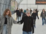 Diwe uczennice liceum jeżdża na łyżwach, trzymają się za ręce. Za nimi na łyżwach jedzie duża grupa osób.