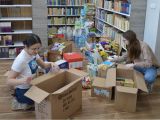 Dwie uczennice liceum siedzą na podłodze i pakują do kartonów produkty spożywcze i środki higieniczne.