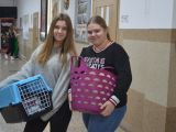 Dwie uczennice liceum stoją obok siebie na korytarzu szkolnym. W rękach jedna trzyma fioletowy kosz, druga kosz dla kota.