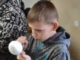 Chłopiec w wieku szkolnym z wielką uwagą maluje pędzlem styropianowe jajo.
