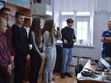 Siedmioro uczniów szkoły podstawowej stoi w rzędzie w klasie. Słuchają mężczyzny, który stoi przed nimi.