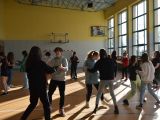 Około dwudziestu uczniów z klasy ósmej szkoły podstawowej tańczy w parach na sali gimnastycznej.