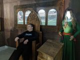 Uczeń w czasnej bluzie siedzi na drewnianym tronie. Obok postać kobiety w zielonej sukni