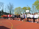 Uczniowie w strojach sportowych stoją w rzędzie na boisku szkolnym.