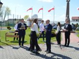 Mężczyzna w garniturze wręcza świadectwo licealistce. Obok stoi kobieta w białym żakiecie. W tle dwoje licealistów.