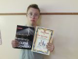 Chłopiec w okularach pozuje do zdjęcia trzymając dyplom i książkę