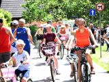 Grupa osób w różnym wieku jedzie na rowerach po chodniku między drzewami.