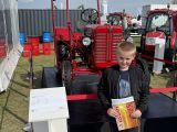 Uczeń szkoły podstawowej w czarnej kurtce. Za nim zabytkowy czerwony ciągnik