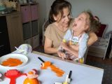 Kobieta w średnim wieku z dziewczynką na kolanach. Przed nimi na stole brystol pomalowany pomarańczową farbą
