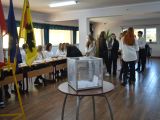 Przy stoliku siedzi pięćioro uczniów liceum. Jedna uczennica pochyla się nad stolikiem i podpisuje kartkę. Obok stoi grupka...