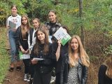 Dziewięć dziewcząt stoi w lesie na skarpie w pobliżu odkrywki glebowej. w rękach trzymają zeszyty szkolne i ołówki