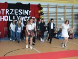 Grupa uczniów liceum w różnych strojach tańczy pośrodku sali gimnastycznej. Na ścianie napis "Otrzęsiny Hollywood".