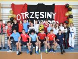Przy ścianie grupa uczniów liceum w strojach sportowych. Drugi rząd stoi, pierwszy siedzi na krzesłach.