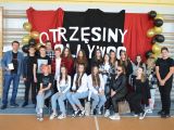 Przy ścianie grupa uczniów liceum, z lewej strony stoi mężczyzna z brodą. Drugi rząd stoi, pierwszy siedzi na krzesłach.