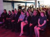 W auli szkolnej uczniowie liceum i nauczyciele siedzą na krzesłach w kilku rzędach. Uczniowie (dzewczyny i chłopcy) w...