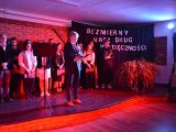 Na scenie w rzędzie stoi grupa uczniów liceum, chłopcy i dziewczyny. Na scęną pada czerwone światło. Pośrodku sceny chłopak...