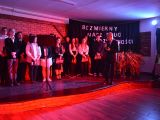 Na scenie w rzędzie stoi grupa uczniów liceum, chłopcy i dziewczyny. Na scęną pada czerwone światło. Pośrodku sceny...