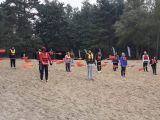 Grupa uczniów liceum stoi na plaży. Wszyscy mają pomarańczowe wiosła. W tle drzwa.