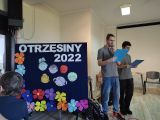 Dwóch gimnazjalistów z granatowymi kartkami w dłoniach. Obok granatowa tablica z napisem Otrzęsiny 2022