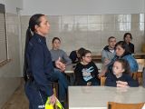 Młoda kobieta w granatowym mundurze. Obok grupa dzieci siedząca na krzesłach