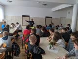 Policjantka w granatowym mundurze. Przed nią duża grupa uczniów siedząca na krzesłach