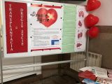Na białej tablicy biały plakat z czarnym tekstem. Obok na czerwonym tle biały napis "Transplantacja = drugie życie". Na...