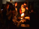 Uczniowie liceum stoją wokół okrągłego stolika, na którym stoją zapalone świece. Losują kartki ze szklanej kuli.