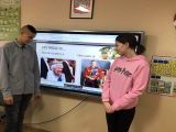 Dwoje gimnazjalistów patrzących na multimedialny ekran z wyświetlonymi zdjęciami króla i królowej
