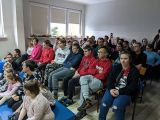 Grupa uczniów siedząca na granatowych materacach. Za nimi duża grupa uczniów siedząca na krzesłach