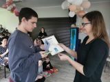 Gimnazjalista w szarej bluzie odbiera dyplom od kobiety w okularach