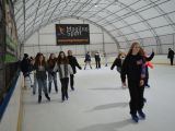 Duża grupa uczniów liceum jeździ na łyżwach po krytym lodowisku. Wszyscy są uśmiechnięci.