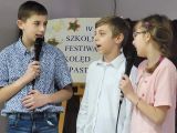 Troje uczniów szkoły podstawowej śpiewa przez mikrofony