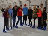 Dziesięcioro licealistów stoi na tafli lodu w rzędzie trzymając się za ramiona. Wszyscy mają łyżwy na nogach.