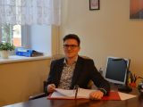 Za biurkiem siedzi uczeń liceum w garniturze i okularach. Przedląda zegregator z dokumentami.