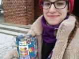 Dziewczyna z liceum w czerwonej czapce w okularach trzyma kolorową tekturowąskarbonkę.
