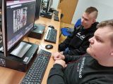 Dwóch gimnazjalistów w czarnych bluzach patrzy w monitor. Na monitorze kolorowe zdjęcia