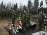 Czworo uczniów w mundurach żołnierskich stoi przy grobie na cmentarzu i pełni wartę.