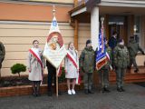 Przed wejściem do szkoły w rzędzie stoi sześcioro uczniów liceum. Dwóch chłopców spośród nich trzyma przed sobą sztandary.