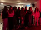 Duża grupa dziewczą z liceum stoi pośrodku sali, jedna z nich trzyma mikrofon i śpiewa. Na sali jest czerwone światło.