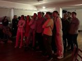 Duża grupa uczniówz liceum stoi pośrodku sali, chłopak trzyma mikrofon i śpiewa. Na sali jest czerwone światło.