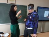 Kobieta ubrana na czarno trzyma buteleczkę przed nosem ucznia w opasce na oczach