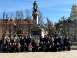 Duża grupa uczniów liceum stoi na placu przed pomnikiem mężczyzny. W tle bordowy budynek.