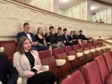 Uczniowie liceum siedzą na czerwonych fotelach w dwóch rzędach w sali teatru.