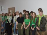 Grupa uczniów liceum stoi przy ścianie na korytarzu. Niektórzy mają zielone bluzy.
