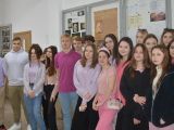 Grupa uczniów liceum stoi przy ścianie na korytarzu. Kilka osób ma różowe koszulki. W tle na ścianie wisi gablota.