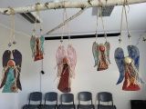 Pięć ceramicznych kolorowych aniołów zawieszonych na brzozowej gałęzi w jasnym pomieszczeniu
