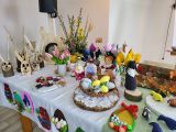Zające z drewna, wielkanocne palmy, pisanki i kolorowe kwiaty z materiału na długim stole przykrytym białym obrusem