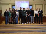 W sali posrodku na podwyższeniu stoi duża grupa uczniów liceum. Za nimi na ścianie wisi ekran projekcyjny.