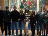 Grupa dziesięciu uczniów liceum stoi w rzędzie w pomieszczeniu. Za nimi ogromny kolorowy obraz.