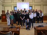 W sali posrodku na podwyższeniu stoi duża grupa uczniów liceum. Za nimi na ścianie wisi ekran projekcyjny.